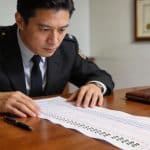 fonctionnaire assis examinant un long tableau chiffré d amendes sur bureau
