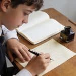 collégien assis à un bureau écrivant une lettre