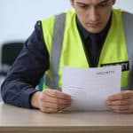 employe en gilet de securite regardant contrat a moitie rempli sur un bureau