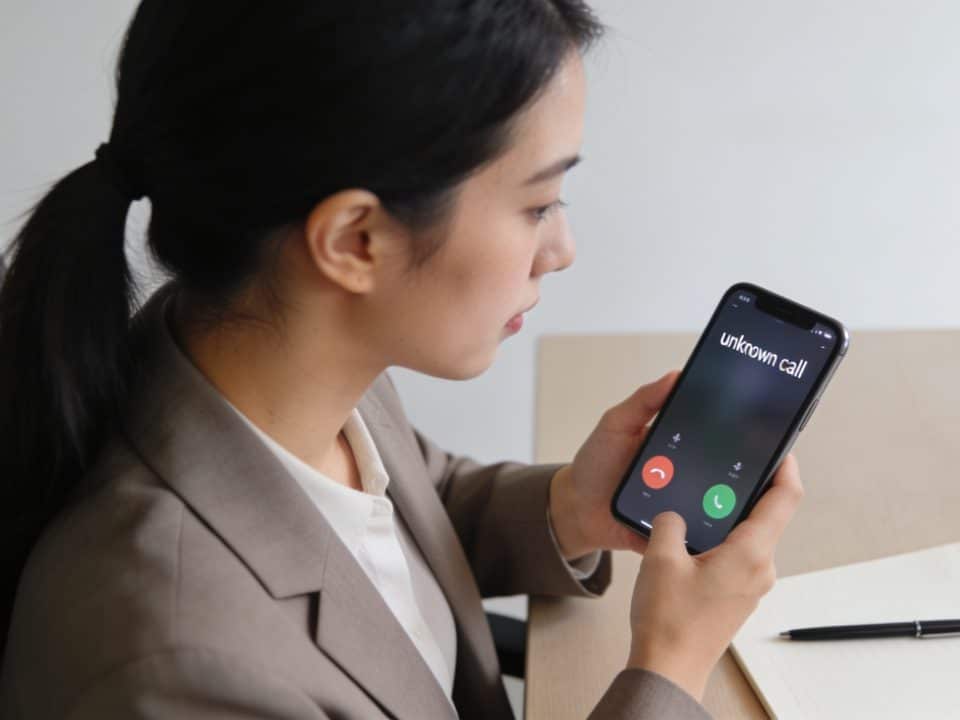 femme assise au bureau regardant smartphone affichant appel inconnu